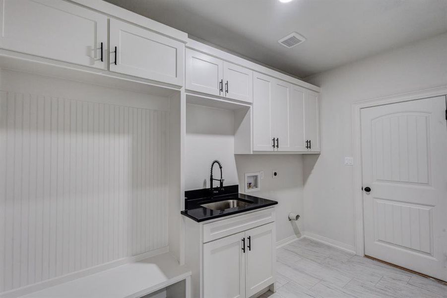 This utility space features white cabinetry with black hardware, a sink with a black faucet, and white beadboard paneling