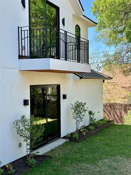 Modern white stucco exterior featuring a second-story balcony with black metal railings, a dark metal standing seam roof accent, and a ground-level sliding glass door