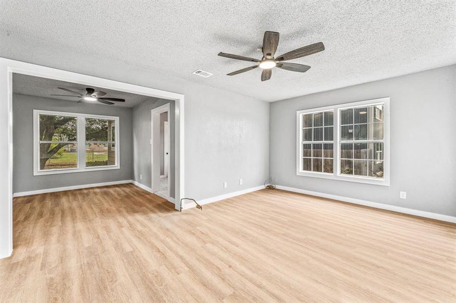 Unfurnished room featuring healthy amount of natural light, light wood-type flooring, ceiling fan, and a textured ceiling Unfurnished room featuring healthy amount of natural light, light wood-type flooring, ceiling fan, and a textured ceiling
