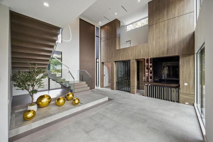 The double-height entry opens to a fabulous wet bar and wine room, setting the tone for luxury and entertaining. A custom pivoting steel front door, imported from Mexico, makes a grand entrance statement. Floating white oak and steel stairs with glass and steel railings provide elegant access to the second floor.