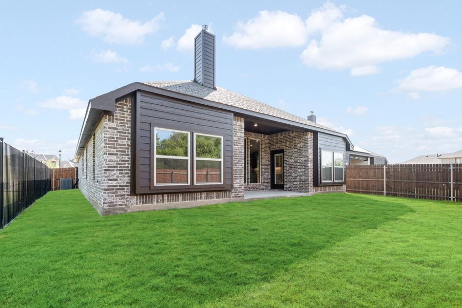 Rear exterior of single-story brick home with covered patio, chimney, and fenced backyard with green lawn.