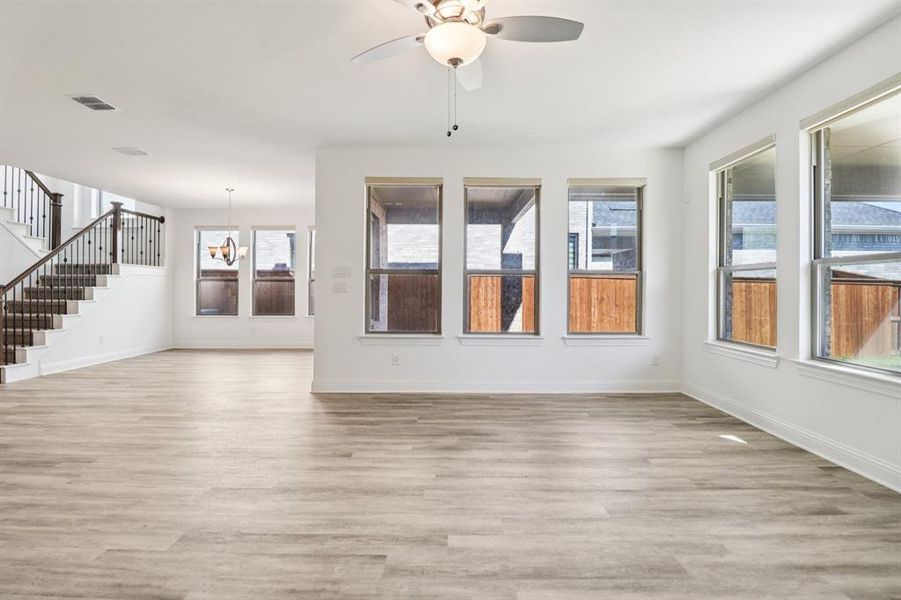 Unfurnished living room featuring stairs, light wood-style flooring, a chandelier, and plenty of natural light Unfurnished living room featuring stairs, light wood-style flooring, a chandelier, and plenty of natural light