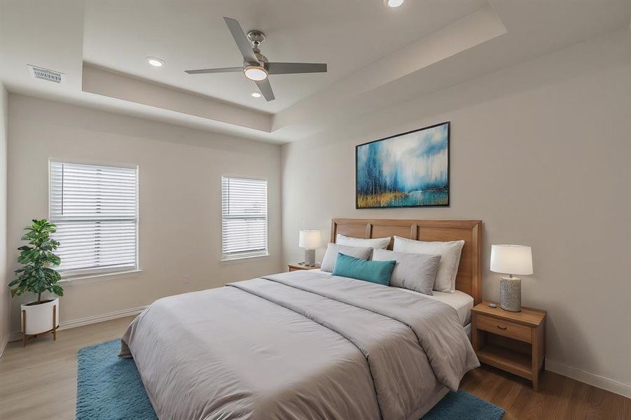 Bedroom featuring a tray ceiling, ceiling fan, and light wood-type flooring