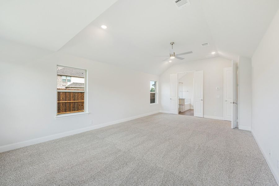 Spacious bedroom with vaulted ceiling, ceiling fan, carpet flooring, and open ensuite bathroom doorway