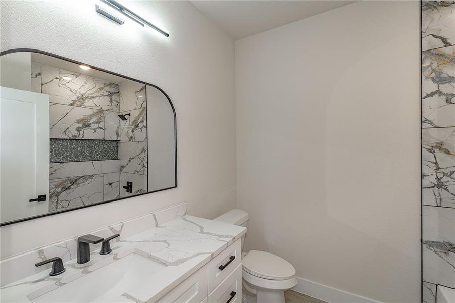 Bathroom featuring toilet, vanity, and a tile shower