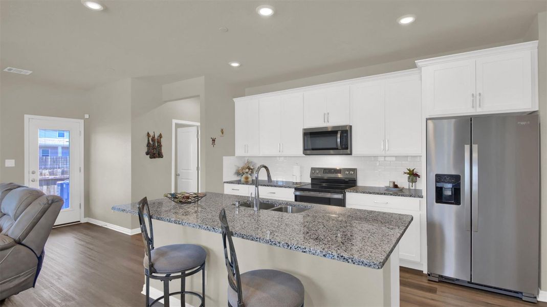 Modern kitchen featuring a breakfast bar with granite countertops, white cabinetry, stainless steel appliances, and wood-finish flooring