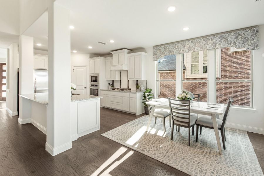 Open-concept kitchen and dining area with white cabinets, granite counters, dark hardwood floors, and large windows