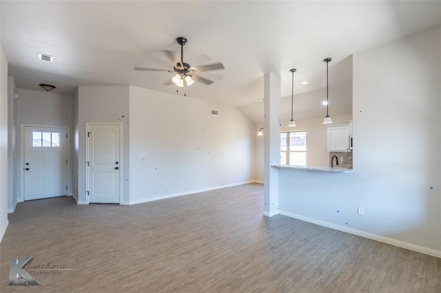Unfurnished living room featuring wood finished floors, a ceiling fan, and vaulted ceiling