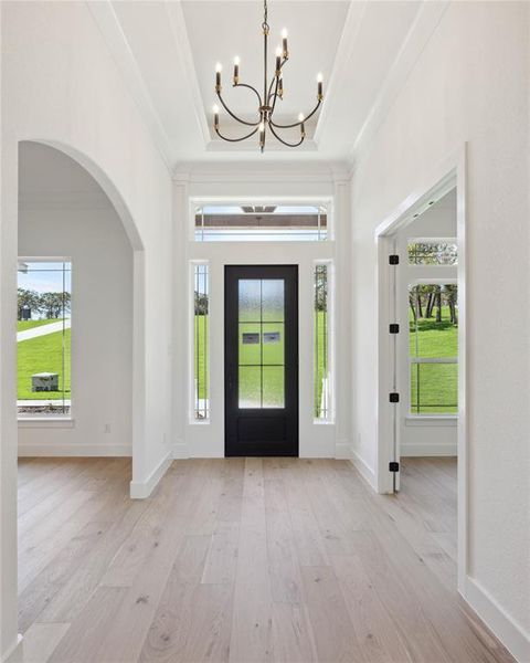 Foyer with ornamental molding, a notable chandelier, light hardwood / wood-style floors, and a raised ceiling