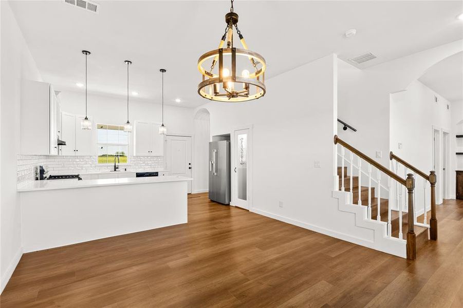 Open-concept living space featuring wood-finish flooring, a contemporary kitchen with white cabinetry and subway tile backsplash, and a staircase with a white baluster and wood handrail