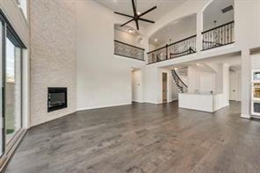 Unfurnished living room featuring dark hardwood / wood-style floors, ceiling fan, a towering ceiling, a large fireplace, and heating unit