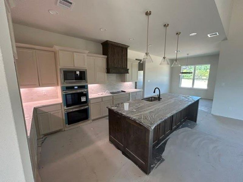 Modern kitchen featuring a large center island with a built-in sink and matte black faucet, pendant lighting, built-in double ovens, and a tile backsplash