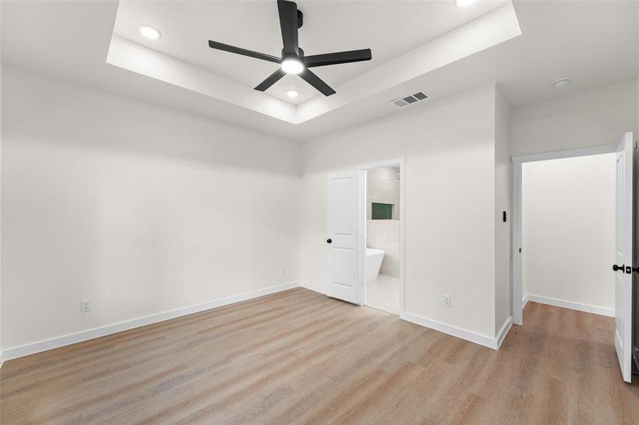 Spacious room featuring wood-finish flooring, a tray ceiling with recessed lighting, and a contemporary black ceiling fan Spacious room featuring wood-finish flooring, a tray ceiling with recessed lighting, and a contemporary black ceiling fan
