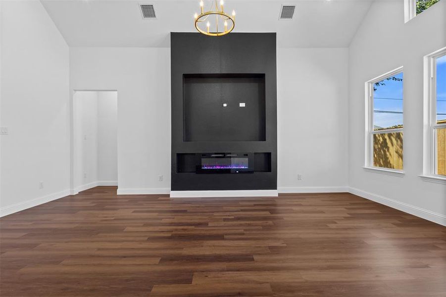 Unfurnished living room with wood finished floors, a glass covered fireplace, lofted ceiling, and a chandelier Unfurnished living room with wood finished floors, a glass covered fireplace, lofted ceiling, and a chandelier