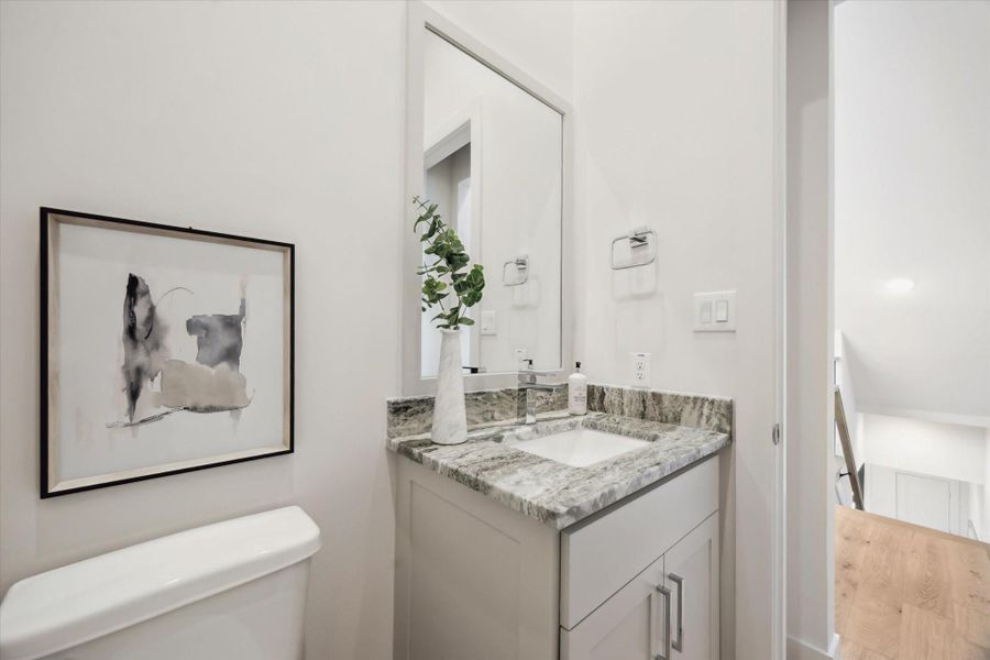This bathroom features a sleek vanity with a marble countertop and modern sink, complemented by a large mirror. A stylish abstract art piece adds a touch of elegance above the toilet. The space is bright and well-lit, showcasing its contemporary design.
