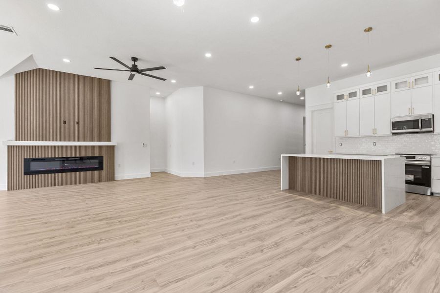 Kitchen featuring open floor plan, glass fronted cabinets, ceiling fan, a glass covered fireplace, and stainless steel appliances