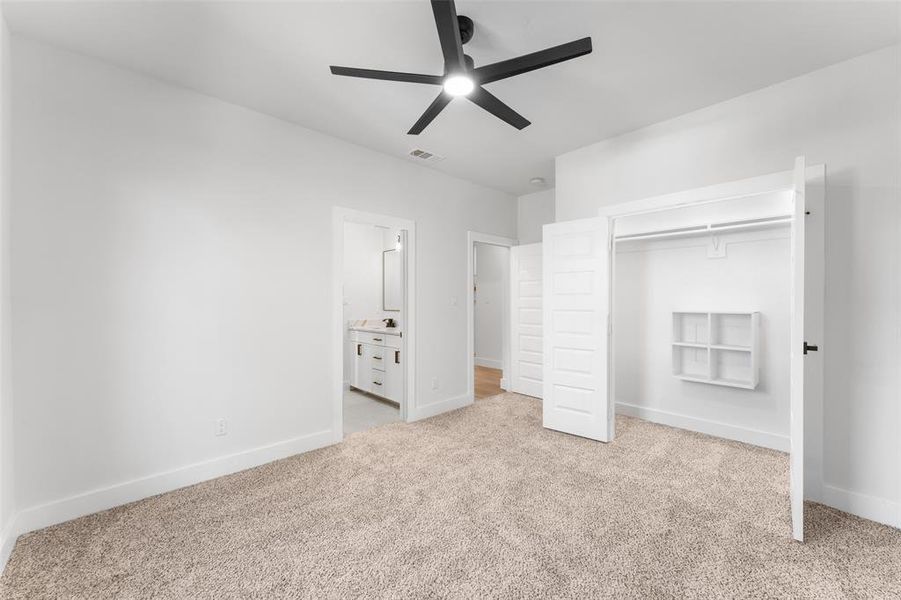 Unfurnished bedroom featuring light carpet, ensuite bathroom, a ceiling fan, and a closet
