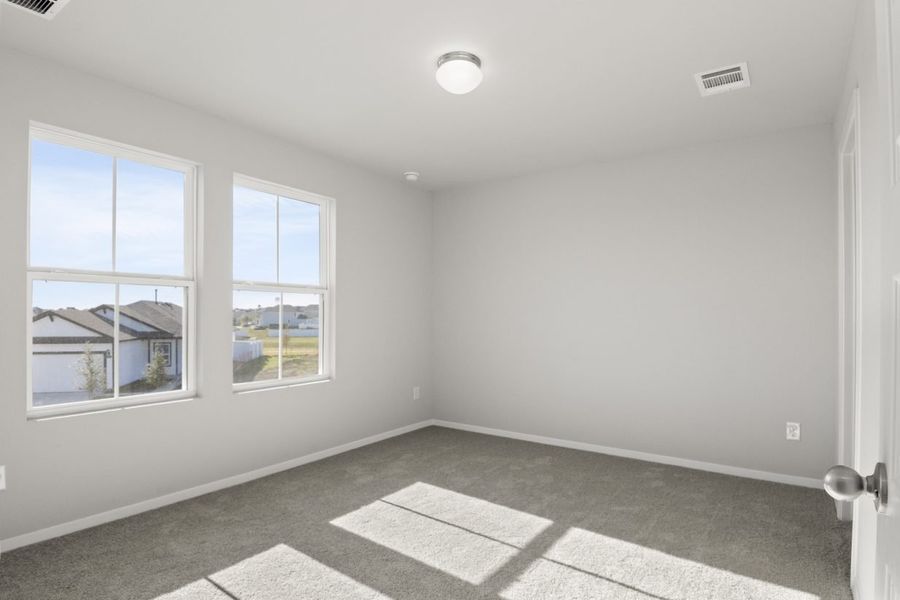 Image of a primary bedroom with light grey walls, tan carpeting and two large windows Image of a primary bedroom with light grey walls, tan carpeting and two large windows