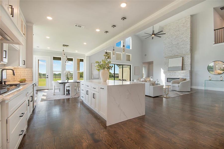Kitchen featuring white cabinetry, decorative light fixtures, a stone fireplace, light stone countertops, and open floor plan Kitchen featuring white cabinetry, decorative light fixtures, a stone fireplace, light stone countertops, and open floor plan