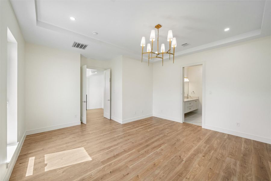 Primary bedroom features wood flooring, recessed lighting, and a stylish modern chandelier. It includes a doorway leading to a bathroom with a vanity, providing a clean and contemporary look.