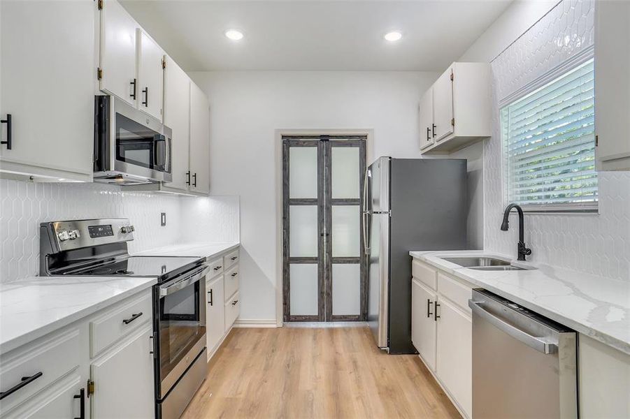 Kitchen featuring white cabinets, stainless steel appliances, light stone counters, and sink