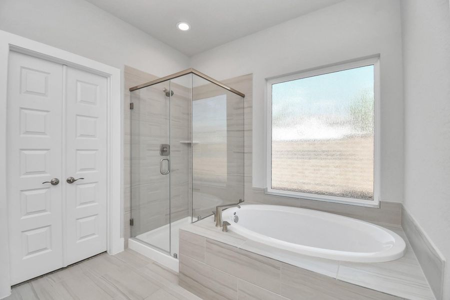 Indulge in a spa-like retreat within the confines of this primary bathroom. Delight in a spacious walk-in shower enveloped in stylish tile surround and unwind in a separate garden tub adorned with custom detailing. Sample photo of completed home with similar floor plan. Actual colors and selections may vary.