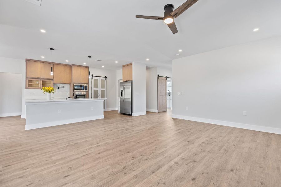 Unfurnished living room featuring light wood-type flooring, a barn door, recessed lighting, and a ceiling fan