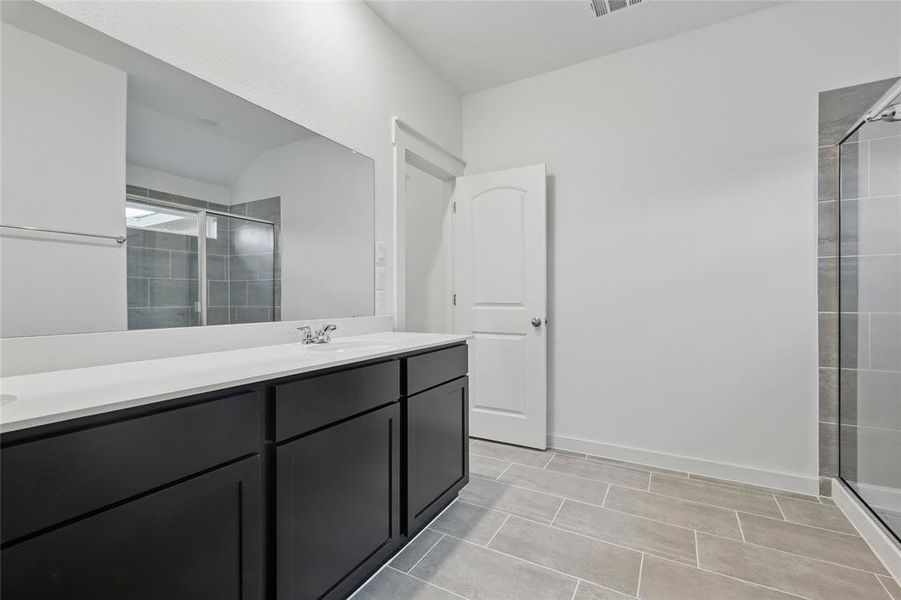 Bathroom featuring a shower stall, double vanity, and light tile patterned floors