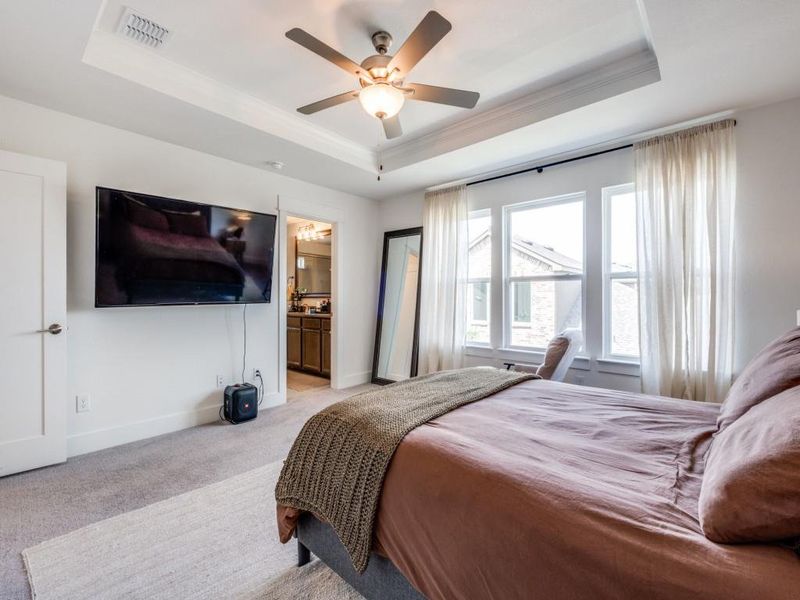 Bedroom featuring a tray ceiling, light carpet, ornamental molding, a ceiling fan, and ensuite bath