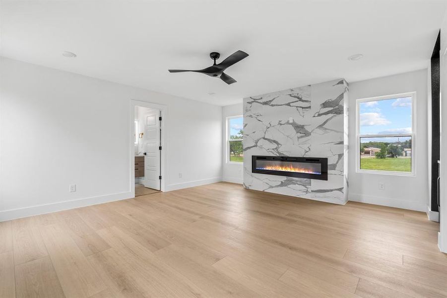 Unfurnished living room featuring light wood-style flooring, baseboards, heating unit, a ceiling fan, and a fireplace