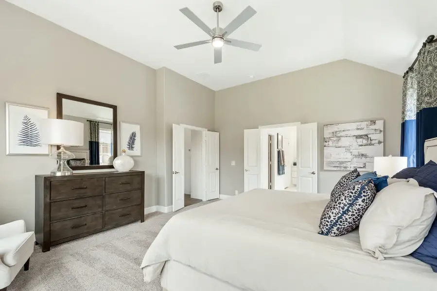 Master bedroom with vaulted ceiling, ceiling fan, carpet floors, and dark wood dresser with mirror