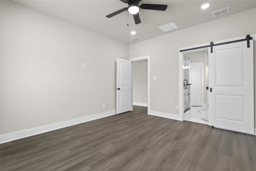 Unfurnished bedroom with ensuite bathroom, a barn door, dark hardwood / wood-style floors, and ceiling fan