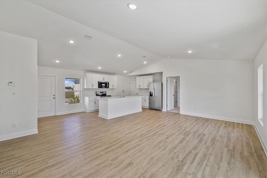 Kitchen featuring open floor plan, vaulted ceiling, stainless steel appliances, light countertops, and white cabinets