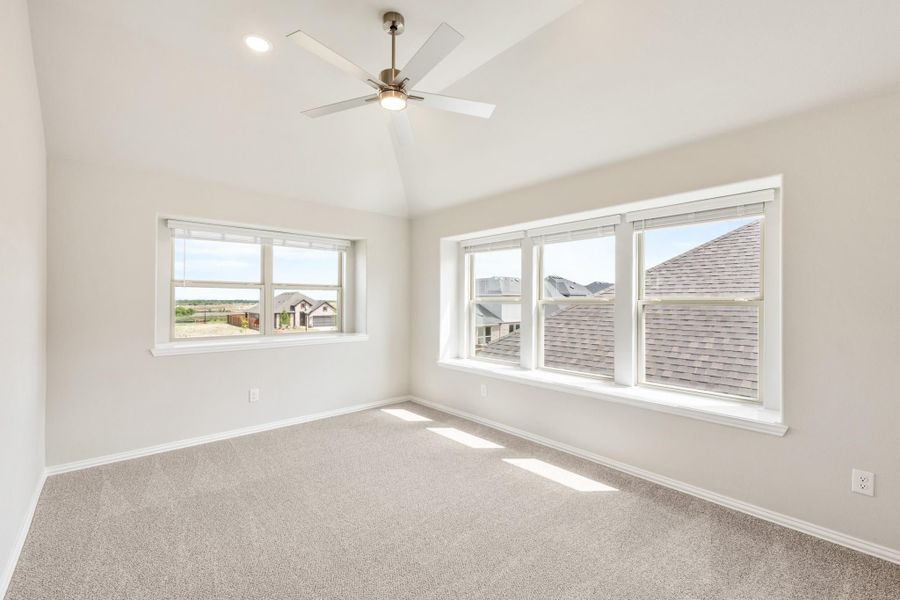 Empty bedroom with vaulted ceiling, ceiling fan, carpet flooring, and large windows with neighborhood views