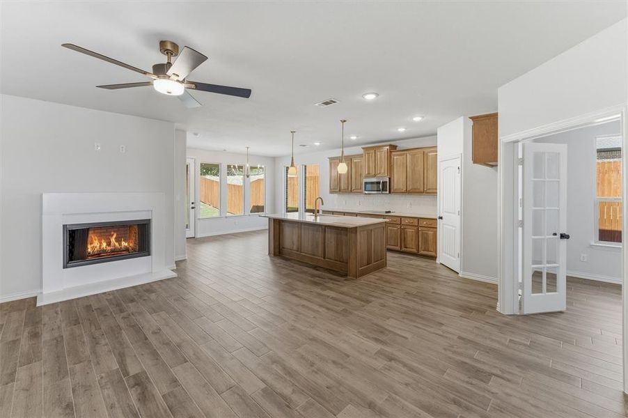 Kitchen featuring open floor plan, light countertops, a glass covered fireplace, an island with sink, and ceiling fan