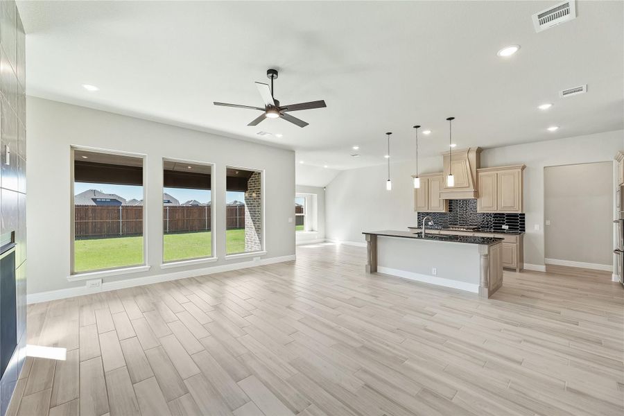 Open-concept living area with light wood floors, ceiling fan, and kitchen island with dark countertops and pendant lights Open-concept living area with light wood floors, ceiling fan, and kitchen island with dark countertops and pendant lights