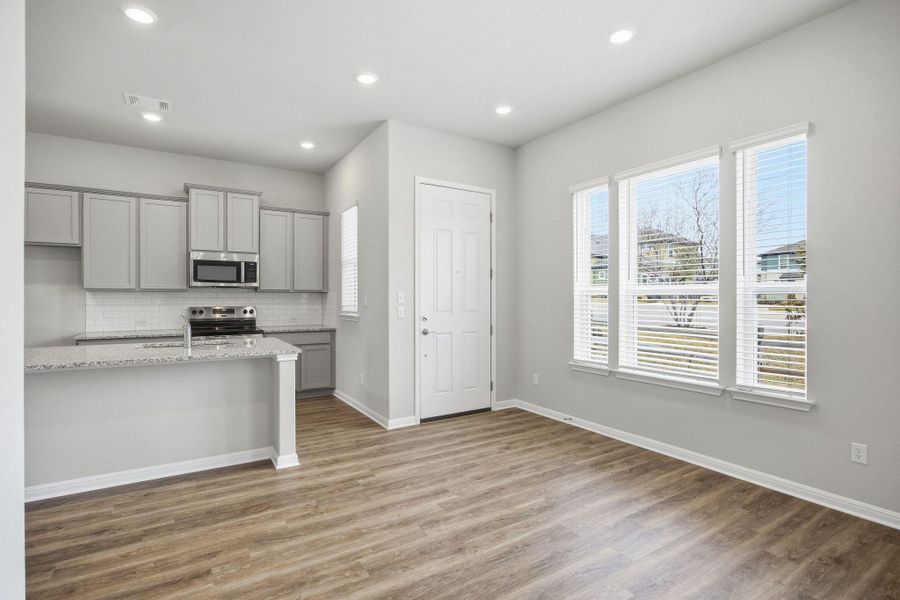 Kitchen with gray cabinetry, backsplash, appliances with stainless steel finishes, light stone counters, and light wood finished floors
