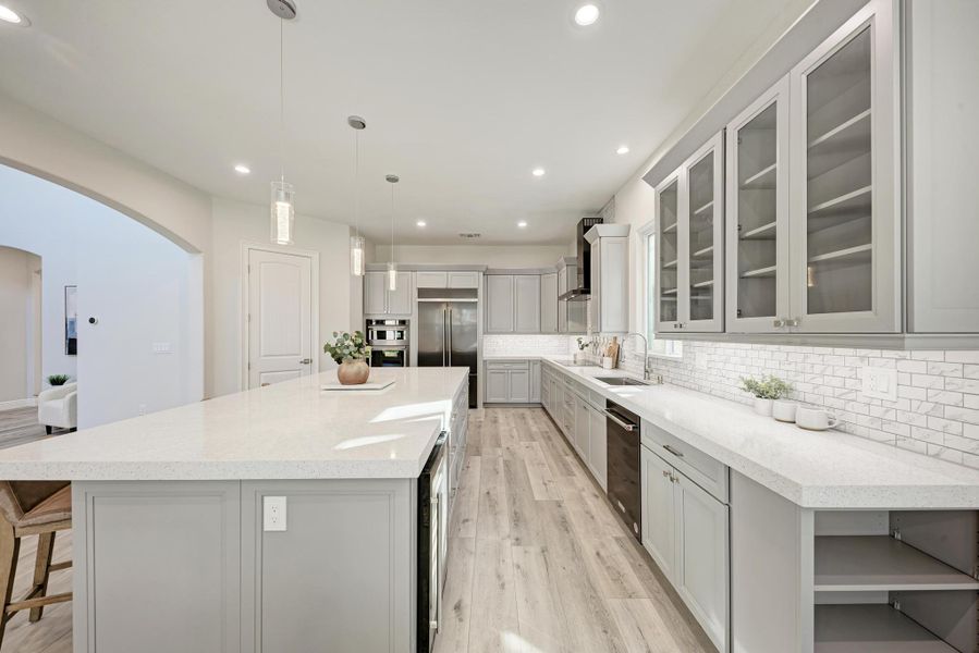 Kitchen with gray cabinets, arched walkways, decorative light fixtures, open shelves, and glass insert cabinets