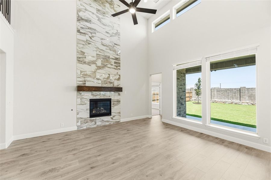 Open living room with two-story stone fireplace, wood floors, ceiling fan, and large backyard windows