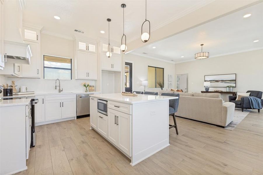 Open-concept kitchen featuring an island with built-in microwave, white cabinetry, integrated stainless steel appliances, and wood-finish flooring