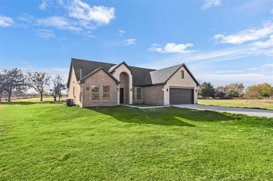 French country inspired facade with a front yard, brick siding, driveway, roof with shingles, and a garage
