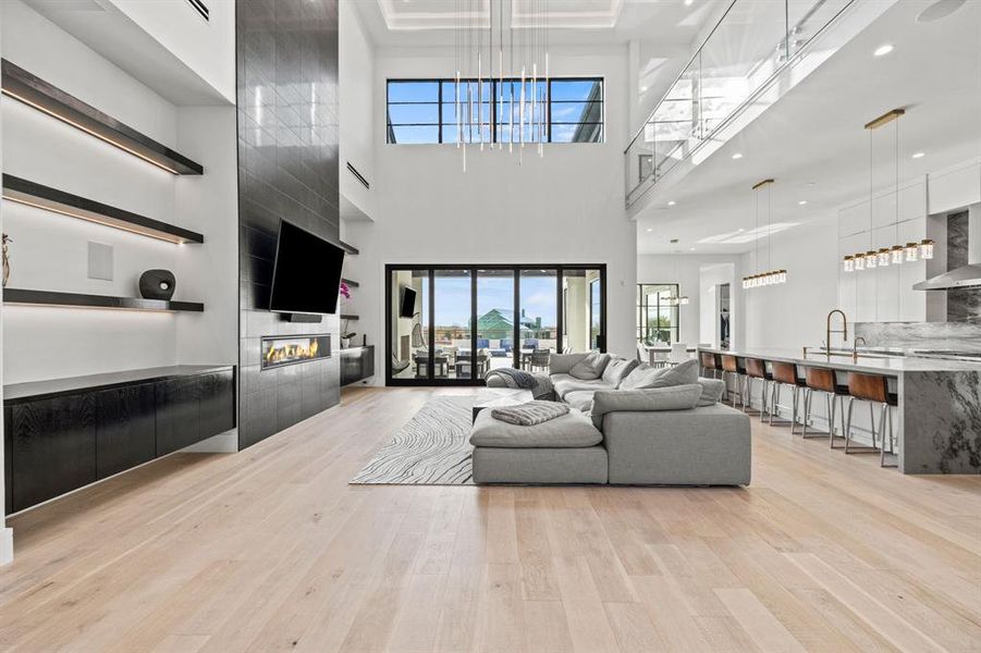 Living room with a high ceiling, sink, light hardwood / wood-style flooring, and a tiled fireplace