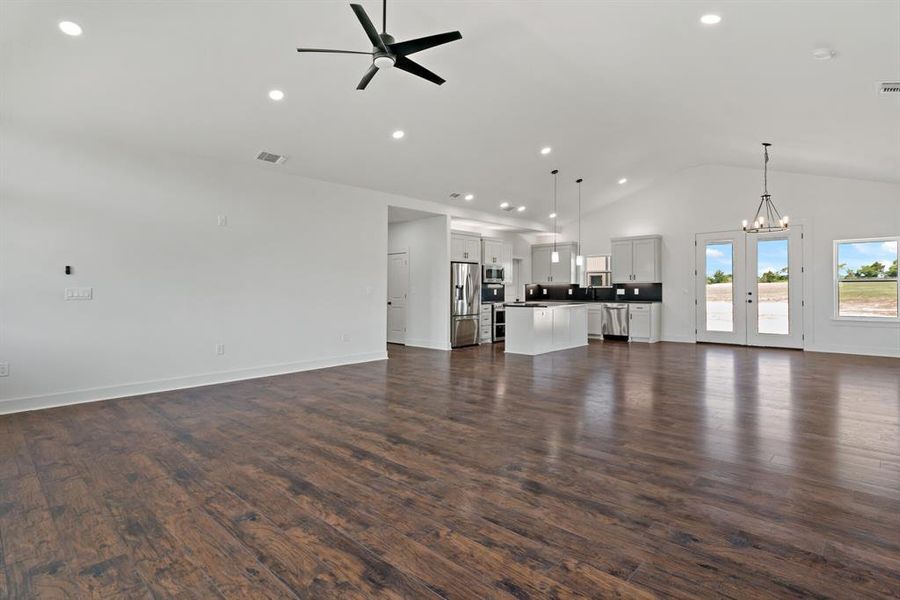 Unfurnished living room with high vaulted ceiling, wood-type flooring, french doors, and ceiling fan with notable chandelier