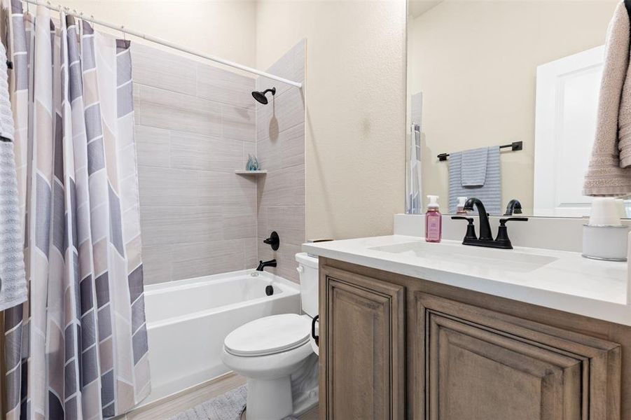 Bathroom featuring a built-in tub with a tile surround, matte black fixtures, a white vanity with shaker-style cabinetry, and a countertop with an integrated sink Bathroom featuring a built-in tub with a tile surround, matte black fixtures, a white vanity with shaker-style cabinetry, and a countertop with an integrated sink