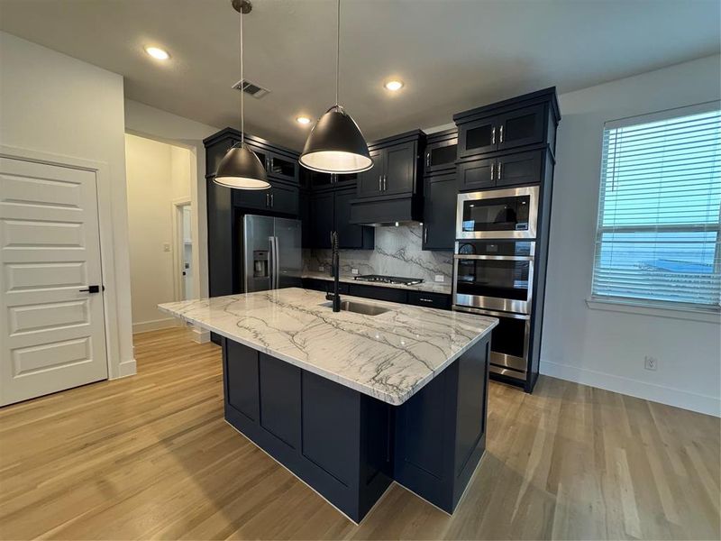 Kitchen with dark cabinetry, visible vents, cooktop, decorative backsplash, and fridge