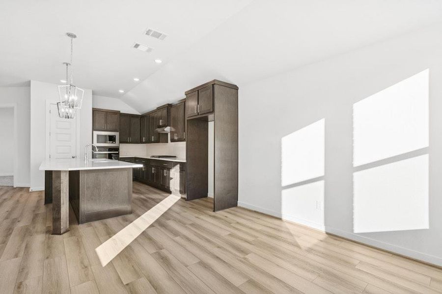 Kitchen featuring dark brown cabinets, lofted ceiling, a kitchen island with sink, hanging light fixtures, and light wood-type flooring Kitchen featuring dark brown cabinets, lofted ceiling, a kitchen island with sink, hanging light fixtures, and light wood-type flooring