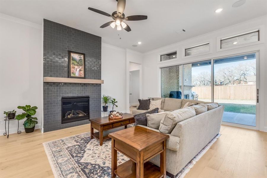 Living room with a tiled fireplace, ceiling fan, light hardwood / wood-style floors, and ornamental molding