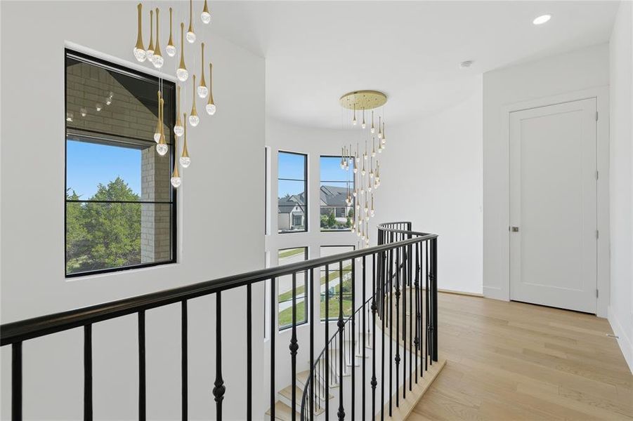Upper-level landing featuring light wood-finish flooring, white walls, and a black wrought-iron railing