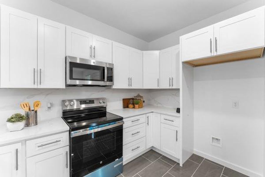 Kitchen featuring appliances with stainless steel finishes, white cabinets, dark tile patterned flooring, and light stone counters Kitchen featuring appliances with stainless steel finishes, white cabinets, dark tile patterned flooring, and light stone counters