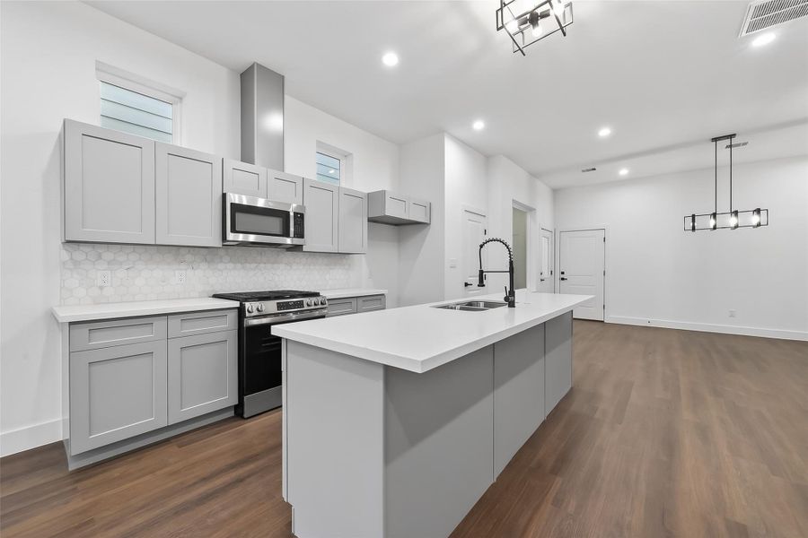 This modern kitchen features sleek gray cabinetry, stainless steel appliances, and a spacious island with a sink. The open layout flows into a bright, airy living area with contemporary lighting and hardwood floors. Perfect for entertaining.